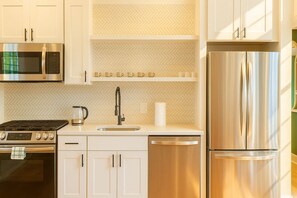A modern kitchen with stainless steel appliances, white cabinetry, and a herringbone tile backsplash.
