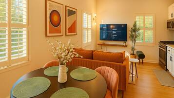 A dining area with a round table, green placemats, a vase with flowers, and a sofa in the background.
