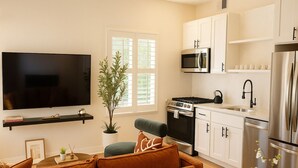 A modern kitchen with white cabinets, stainless steel appliances, a flat-screen TV, and a comfortable seating area with a sofa and a coffee table.