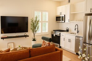 A modern kitchen with white cabinets, stainless steel appliances, a flat-screen TV, and a comfortable seating area with a sofa and a coffee table.