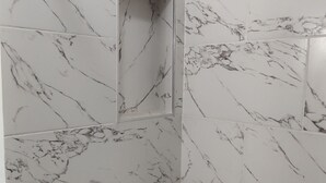 Une salle de bain avec une baignoire blanche, un espace douche doté d’une porte en verre et un mur décoré d’un motif imitant le marbre.