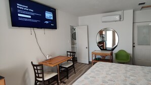 Une chambre d’hôtel équipée d’un lit, d’un bureau avec des chaises, d’un miroir, d’une armoire et d’un téléviseur affichant un message de bienvenue.