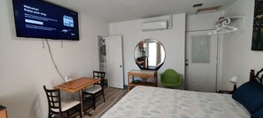 A hotel room with a bed, a desk with chairs, a mirror, a wardrobe, and a television displaying a welcome message. - Comfy Studio by Baseball Stadium. Own Entrance (Miami)