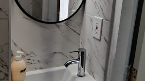 Une salle de bain avec un lavabo en marbre, un miroir rond et deux appliques murales.