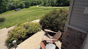 Un patio con dos sillas de madera y una mesita, con vistas a un paisaje verde exuberante y un edificio distante.