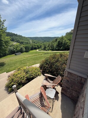 A patio with two wooden chairs and a small table, overlooking a lush green landscape and a distant building.