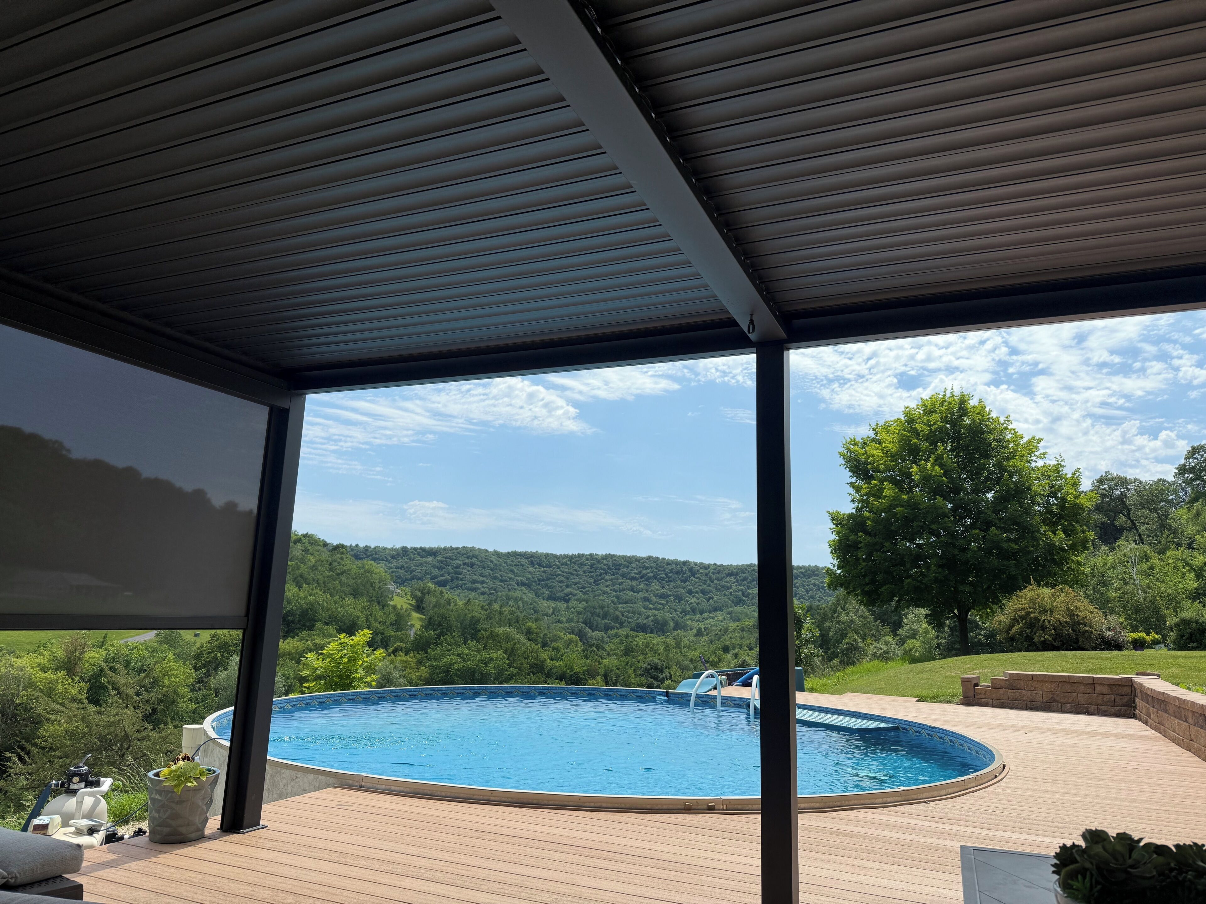 Un espace extérieur abrité comprenant une piscine, une terrasse en bois et une vue sur une colline boisée.