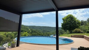 Un espacio al aire libre cubierto con piscina, muelle de madera y vistas a una ladera boscosa.