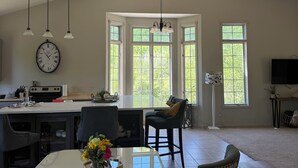 Una cocina amplia con una isla grande, un comedor con mesa de vidrio y una sala de estar con sofá y televisor.