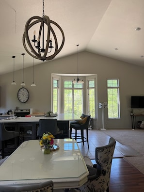 A spacious kitchen with a large island, a dining area with a glass table, and a living room with a sofa and a TV.