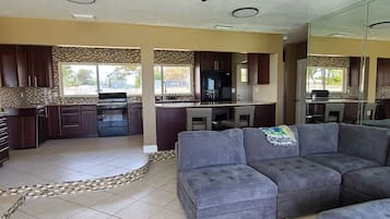 A modern kitchen with dark cabinets, a central island, and a dining area with a gray sofa.
