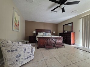 A bedroom with a bed, a dresser, a chair, a ceiling fan, and a window with blinds. - Cozy Getaway with a Dock Facing Rocket Launch Facilities Across the Indian River (Titusville)