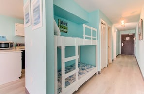 Una habitación con literas, una zona de cocina y un pasillo que conduce a una puerta.