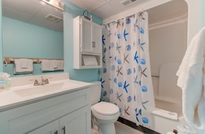 Un baño con un lavabo blanco, inodoro, cortina de ducha con criaturas marinas y un espejo sobre el lavabo.