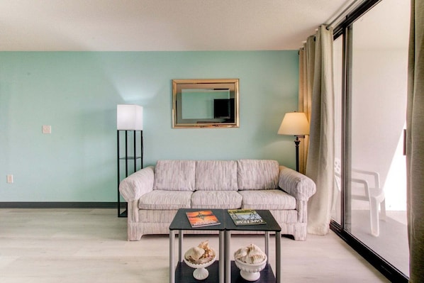 Una sala de estar con pared azul claro, un sofá, una mesita con dos cuencos, una lámpara de pie y un espejo.