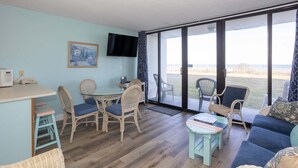 Una habitación con una mesa de comedor, sillas, un sofá, un televisor y ventanas grandes.