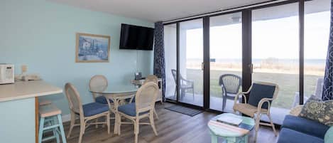 A room with a dining table, chairs, a sofa, a television, and large windows.
