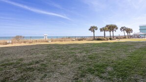 Vista a la playa con una torre de salvavidas, palmeras y un edificio con terraza.