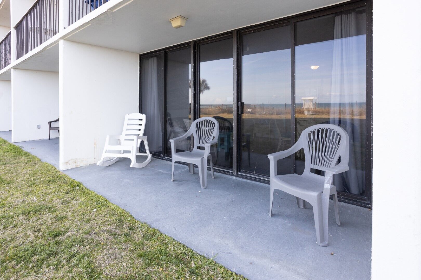 A modern building with a balcony, white plastic chairs, and a view of the ocean.