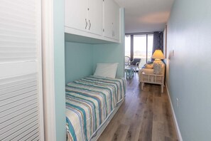 Una habitación pequeña con una cama, una mesita, una silla y una lámpara.