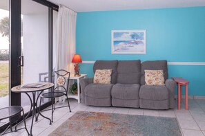 A living room with a sofa, a small table, a chair, a lamp, and a painting on the wall.