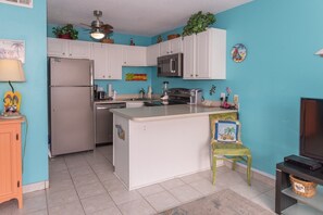 A compact kitchen with white cabinets, a refrigerator, a microwave, and a small island.