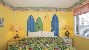 A bedroom with a bed, two nightstands, a window with blinds, and a tropical-themed wall mural. - Cozy 1BR oceanfront condo in Carolina Beach 0201 (Carolina Beach)