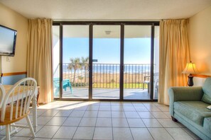 A room with a balcony, a TV, a sofa, and a dining table. - Oceanfront escape: 2BR, 2BA condo at Carolina Beach, perfect for a family getaway! (Carolina Beach)