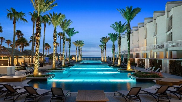 A swimming pool with lounge chairs and palm trees, surrounded by hotel buildings.