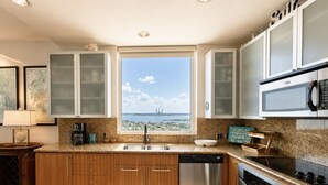 A kitchen with wooden cabinets, a stainless steel dishwasher, a built-in oven, and a large window with a cityscape view.