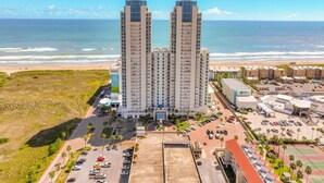 A high-rise hotel with a beach view, parking area, and adjacent buildings.