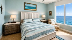 A bedroom with a bed, nightstands, a ceiling fan, a window with a view of the ocean, and a painting on the wall.