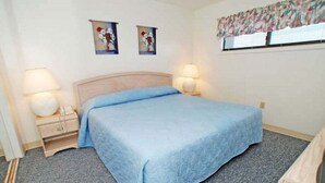 A bedroom with a bed, two bedside tables with lamps, and two wall-mounted paintings.