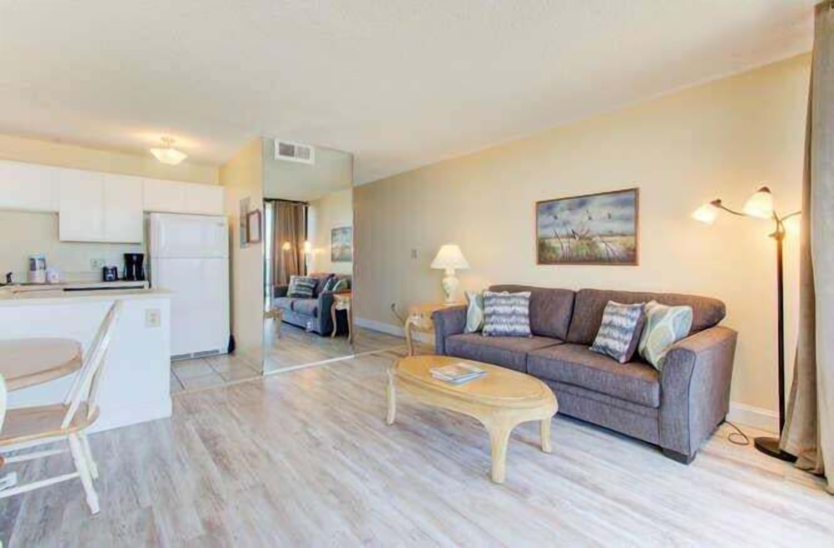 A modern living room with a sofa, coffee table, and a dining area with a kitchen in the background.