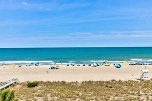 Ein Strand mit Sonnenschirmen und Liegestühlen, einem Rettungsturm und blauem Himmel.