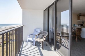 En balkon med udsigt over stranden, et bord med stole og et tekøkken.