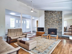 A living room with a stone fireplace, a sofa, a television, and a patterned rug.