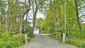 Ein gepflegter Schotterweg führt zu einem weißen Gebäude mit Garage, umgeben von Bäumen und Grün.