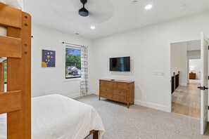 Ein Schlafzimmer mit einem Bett, einer Kommode, einem Fernseher und einem Fenster mit Blick auf ein Haus.