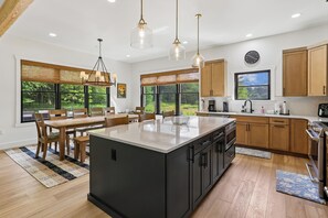 A modern kitchen with a large island, wooden cabinets, and a dining area with a view of the outdoors. - Experience luxury at Summit and Shore, a 5-bedroom retreat in beautiful Swanton, MD. (Swanton)