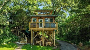 Uma casa na árvore de madeira com escada, cercada por vegetação exuberante.
