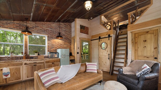 Interior rústico de uma cabana com piso de madeira, um sofá, uma cadeira, uma área de jantar e uma cozinha.