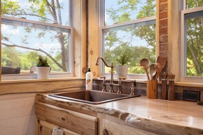 Une cuisine dotée d’un plan de travail en bois, d’un évier et de deux fenêtres donnant sur la forêt.