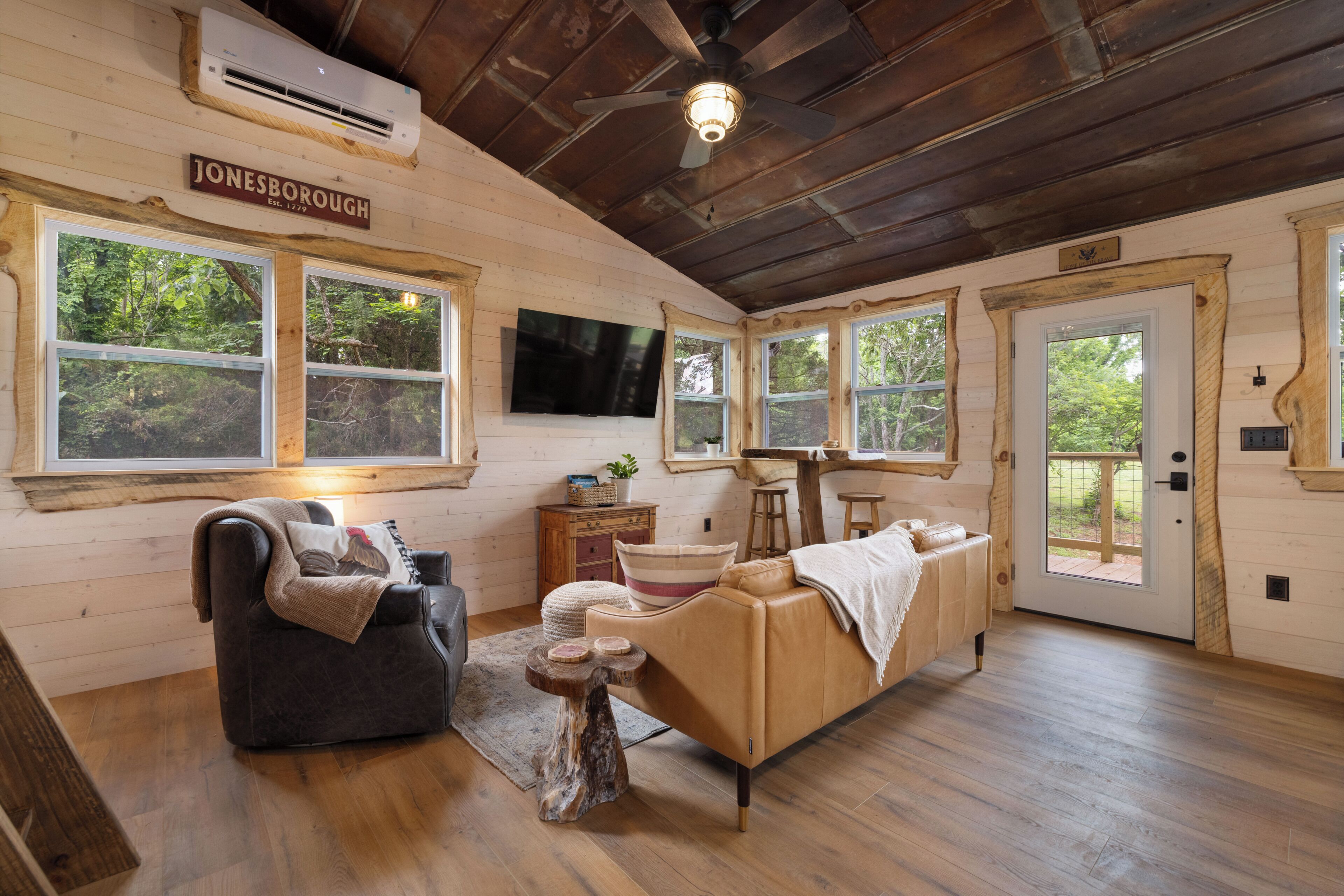 A log cabin interior with a sofa, a chair, a small table, a TV, and a door leading outside.. "Treedom", Treehouse with a Disc Golf Course, Hot Tub, Arcade, Firepit and Slide