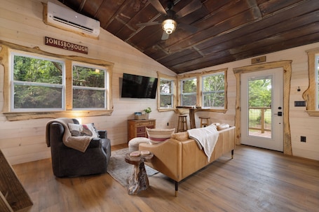 A log cabin interior with a sofa, a chair, a small table, a TV, and a door leading outside.. "Treedom", Treehouse with a Disc Golf Course, Hot Tub, Arcade, Firepit and Slide