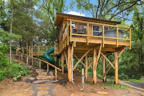 A wooden elevated structure with a staircase and a slide, surrounded by trees.