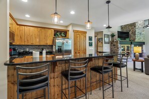 Eine moderne Küche mit Holzausstattung, einem Edelstahlkühlschrank und einer Bar mit Hockern.