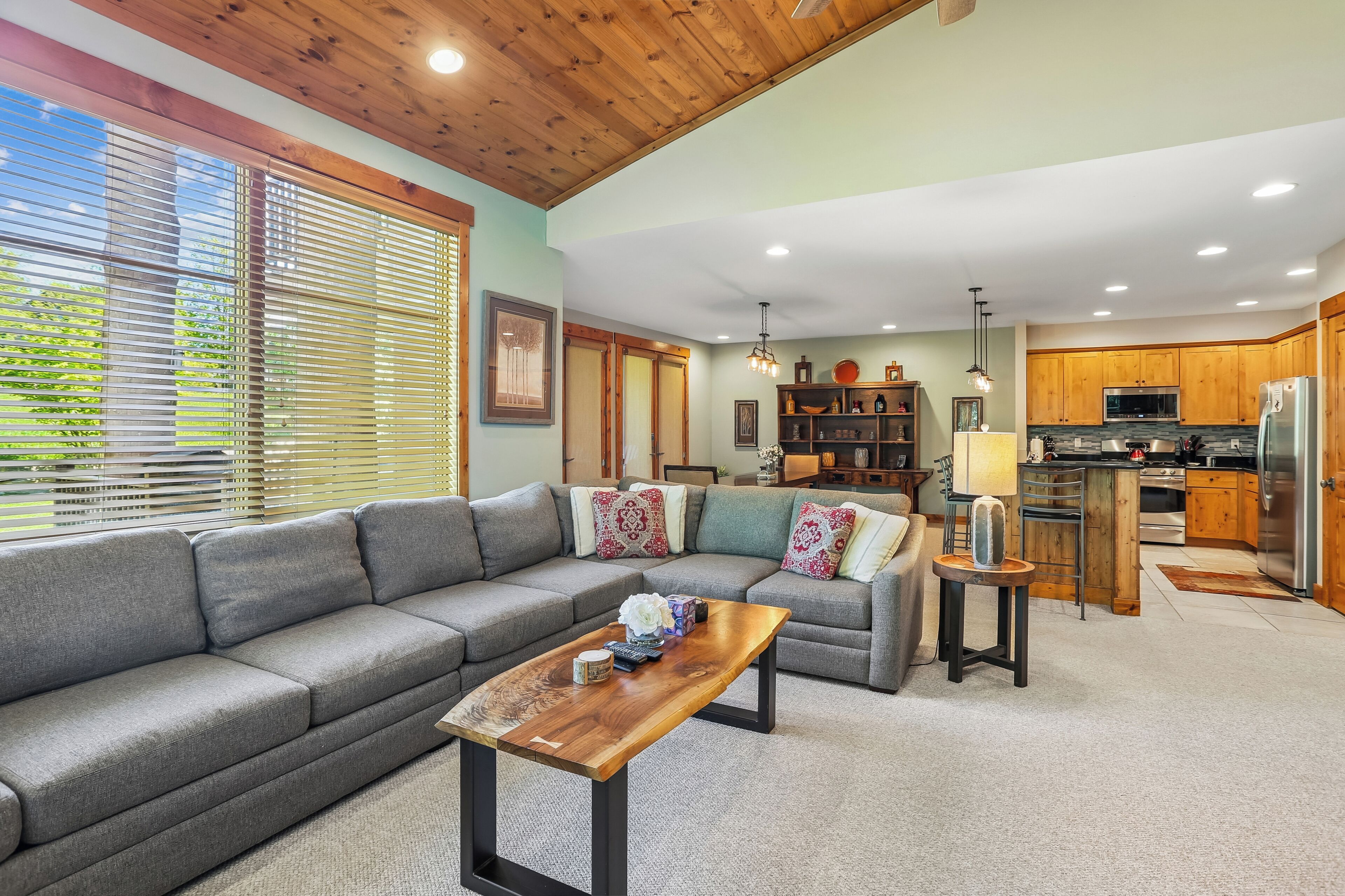 A modern living room with a grey sofa, wooden coffee table, and a kitchen in the background.
