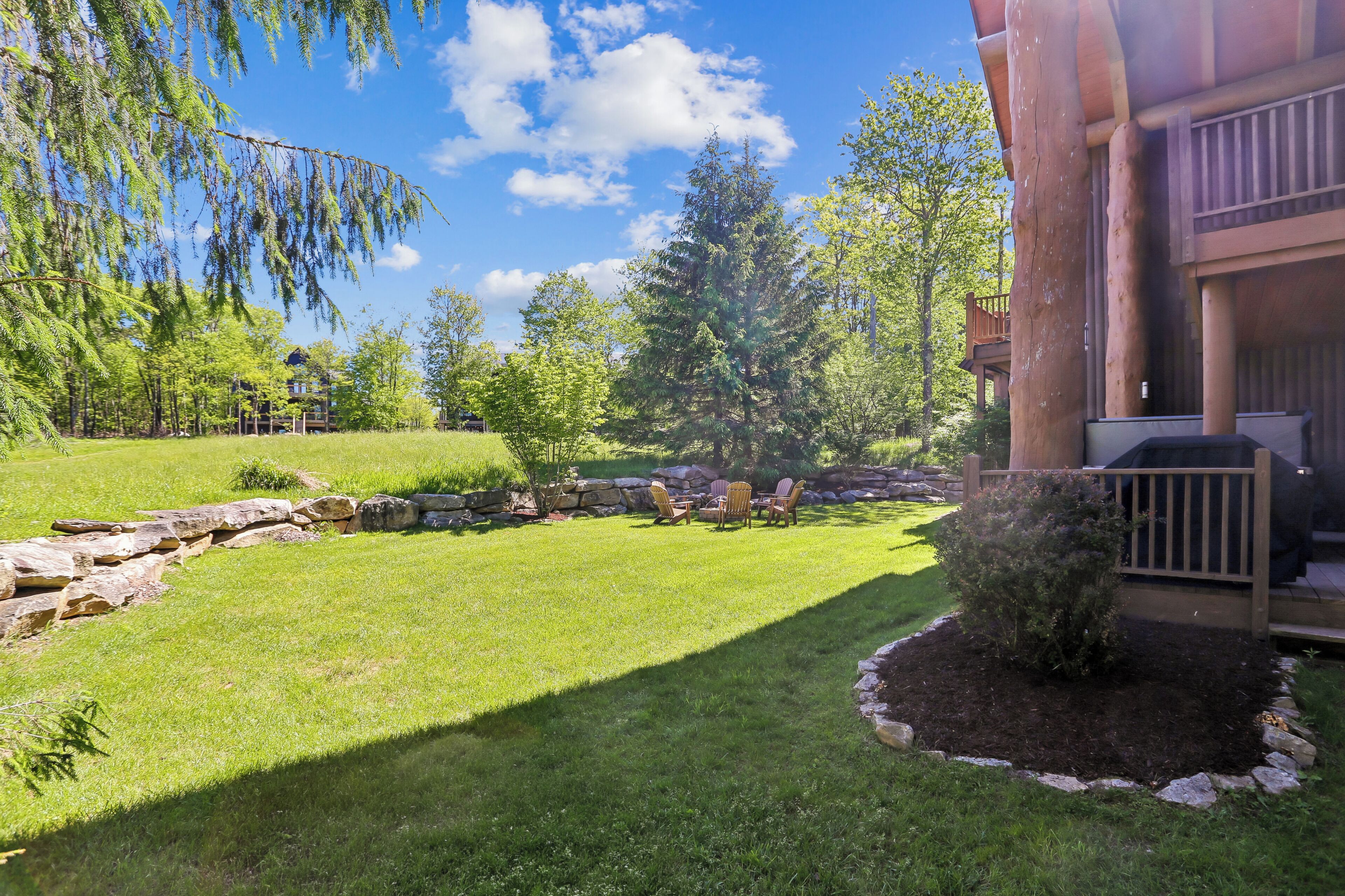 A well-maintained lawn with a stone retaining wall, a small bush, and a grill area.