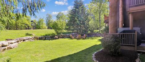A well-maintained lawn with a stone retaining wall, a small bush, and a grill area.